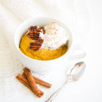 Close up of a pumpkin spice mug cake topped with whipped cream and pecans.