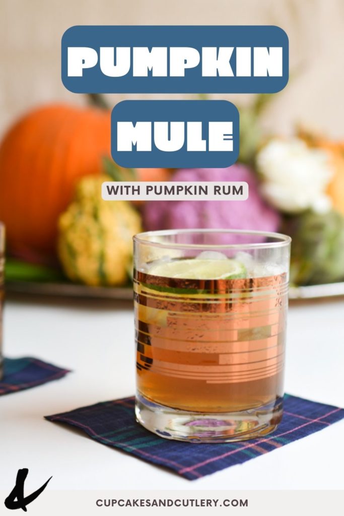 A cocktail glass with a fall centerpiece behind it and text that says "Pumpkin Mule".