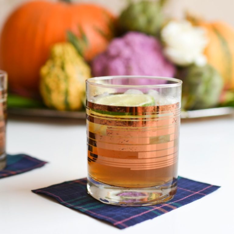 A cocktail glass with a Pumpkin Mule in it with a holiday centerpiece in the background.