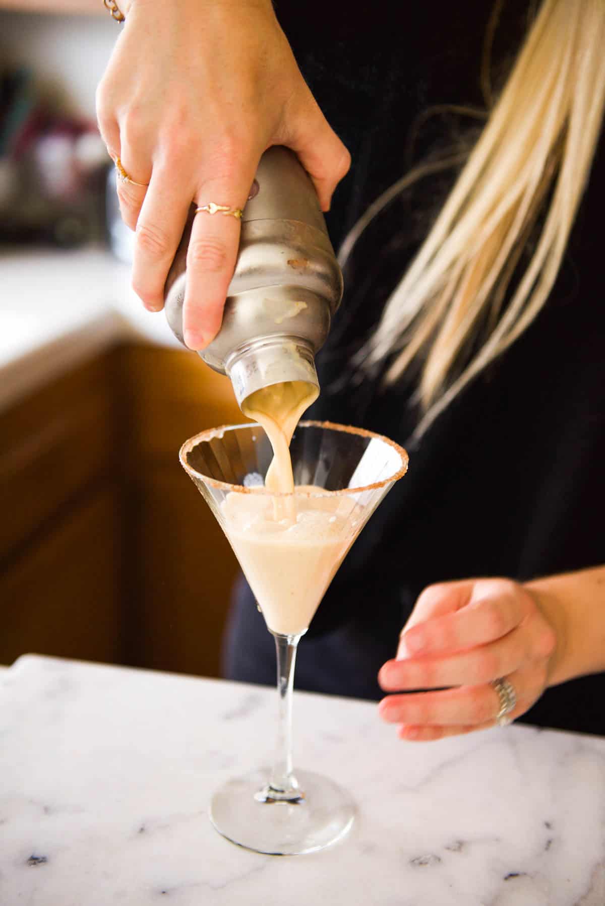 Pouring a pumpkin martini from a cocktail shaker into a martini glass.