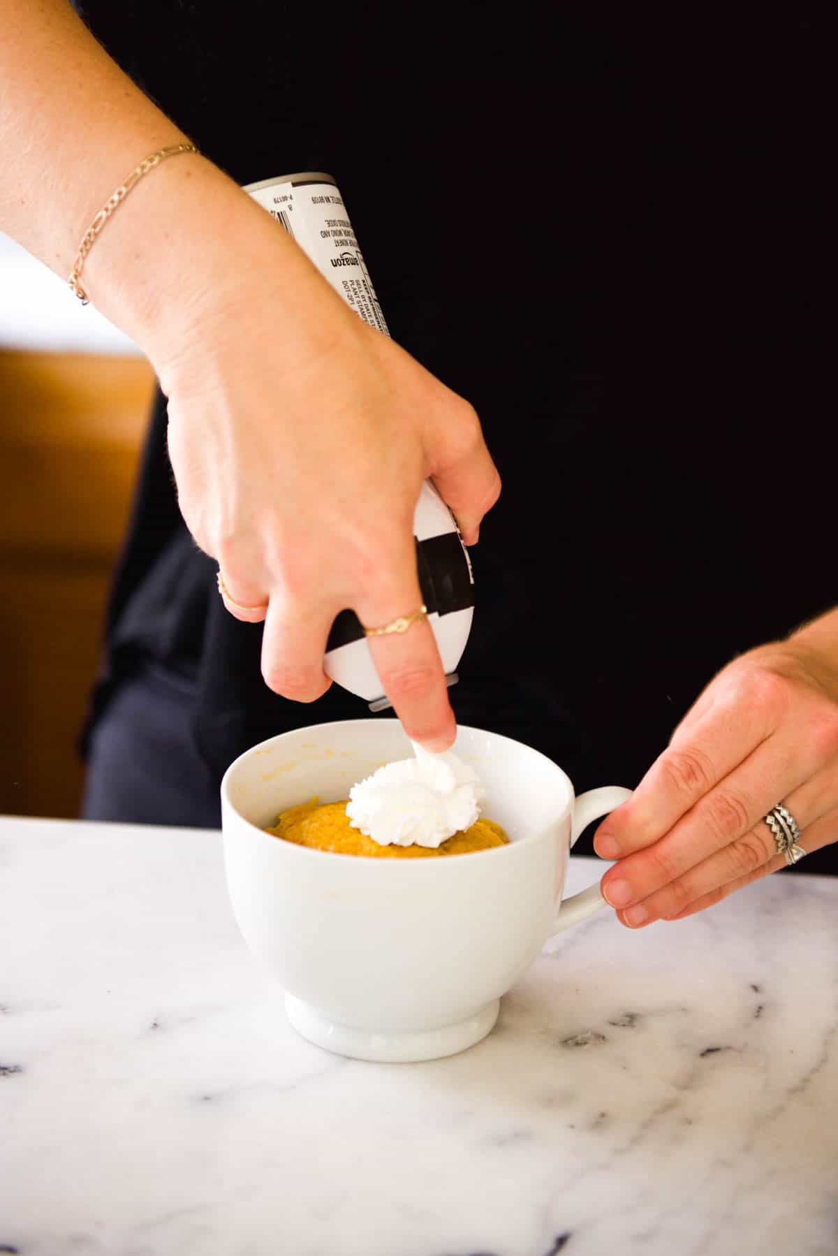 Adding whipped cream to the top of a pumpkin mug cake.