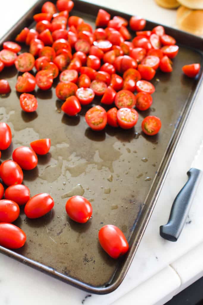 Cherry tomatoes on a sheet pan with some of them cut in half.