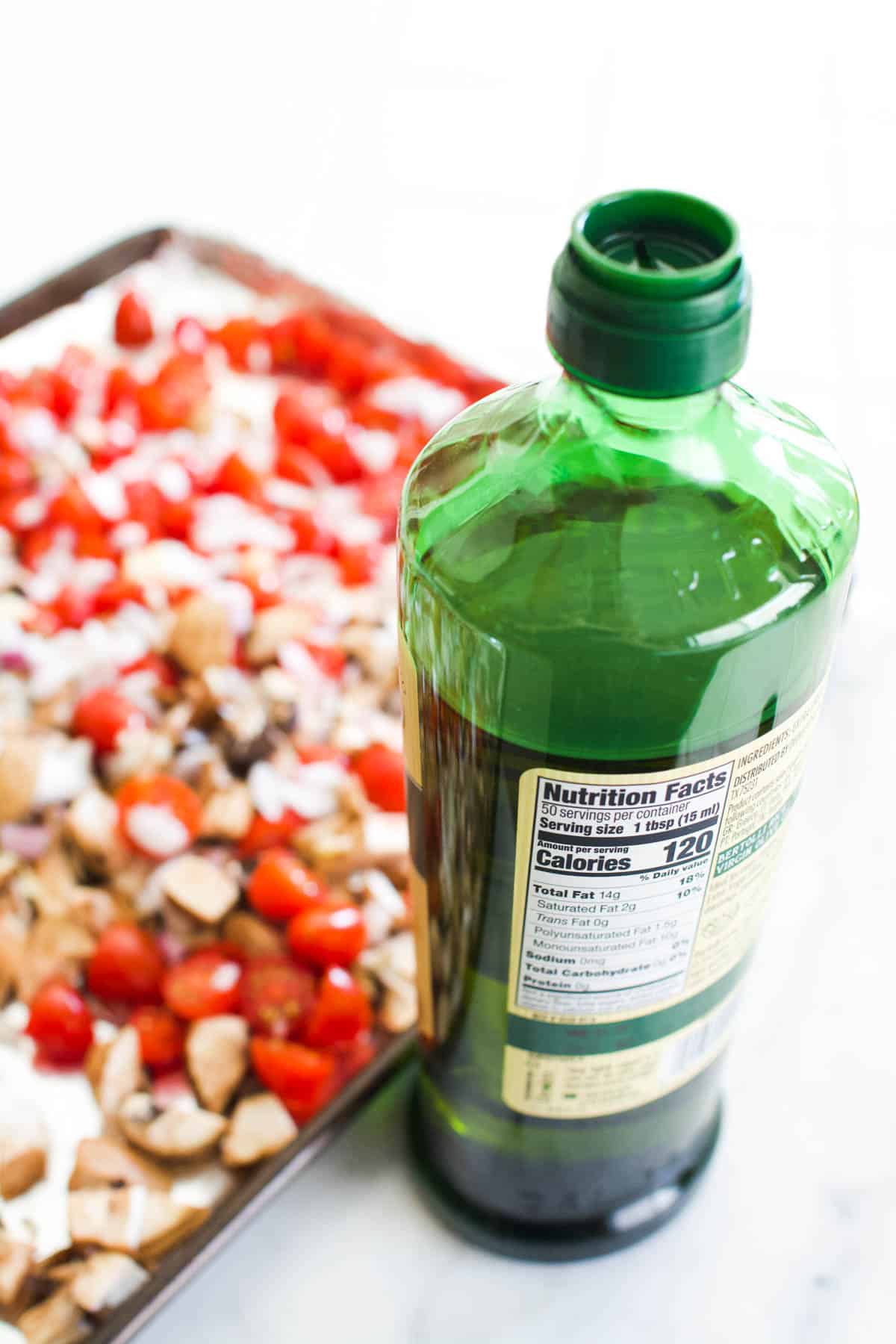A sheet pan with tomatoes and mushrooms next to a bottle of olive oil.