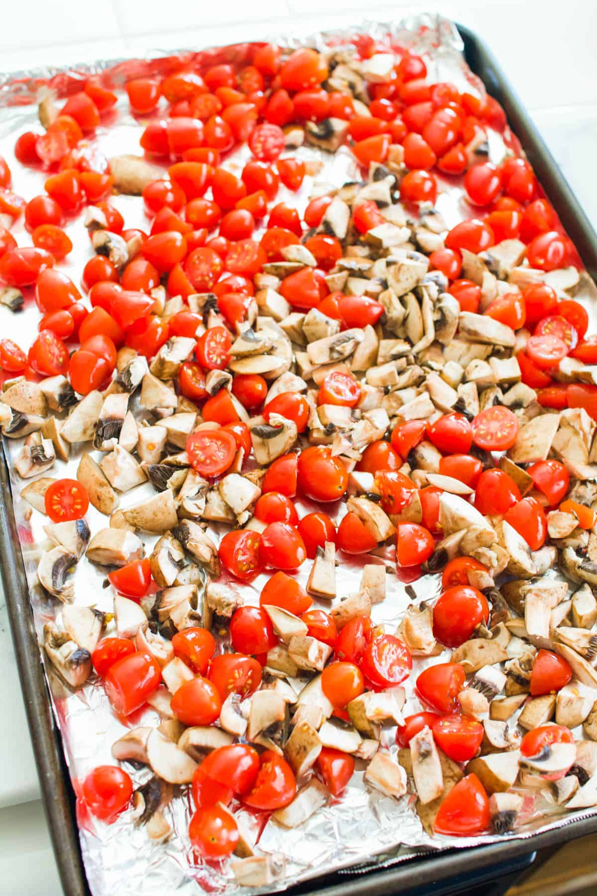 A sheet pan with cherry tomatoes and chopped mushrooms.