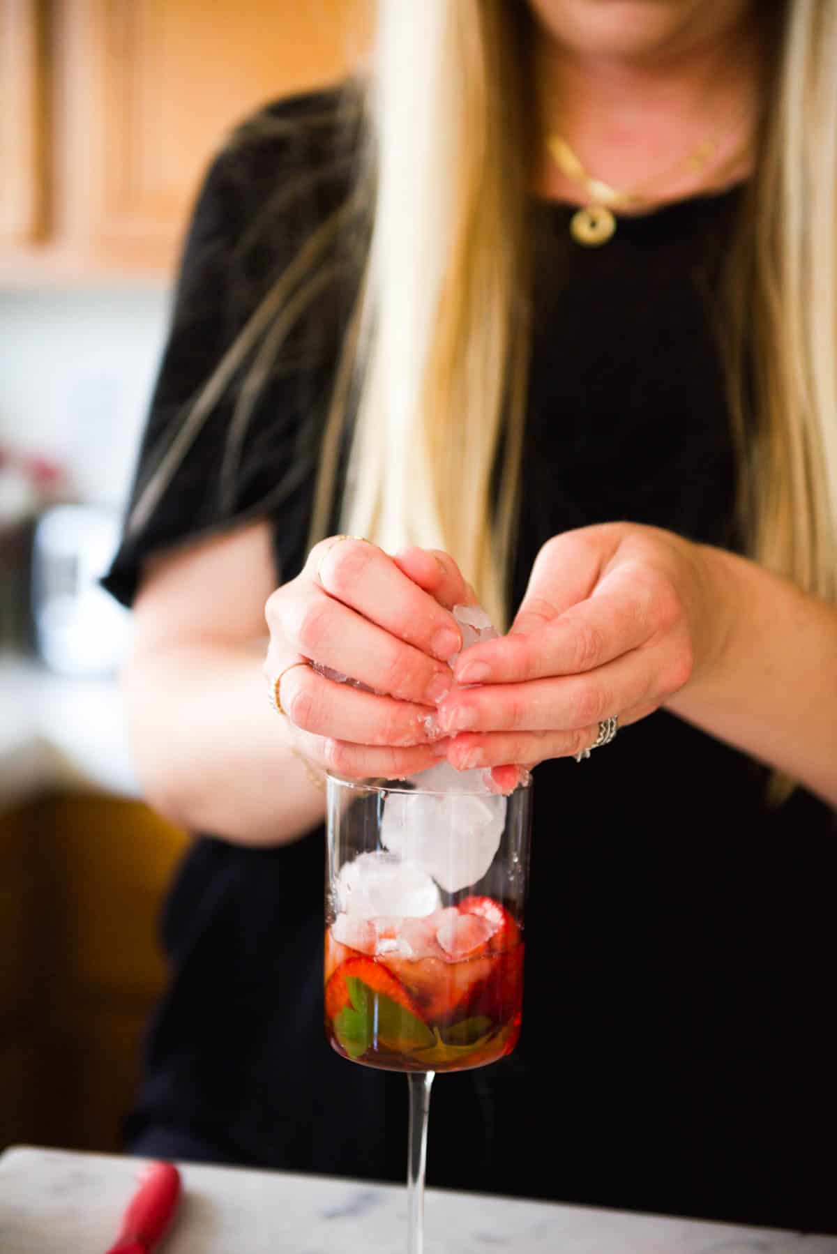 Woman adding ice to a wine glass for a cocktail.