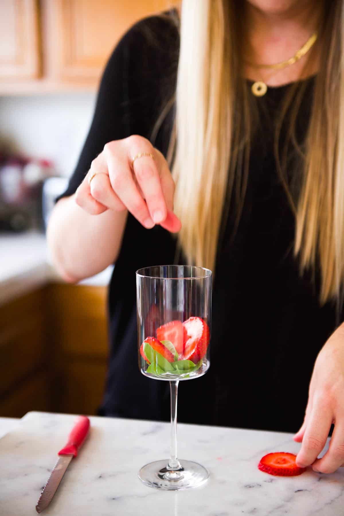 Adding sliced fresh strawberries to a wine glass for a drink recipe.