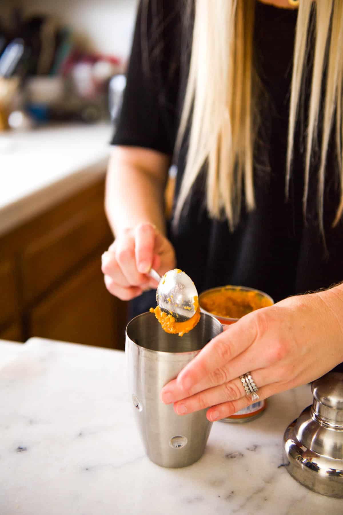 Adding a scoop of canned pumpkin to a cocktail shaker for a martini.