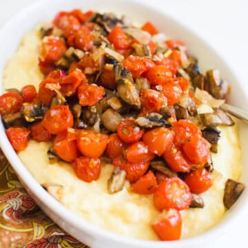 Close up of a white serving dish with creamy polenta topped with roasted mushrooms and tomatoes.