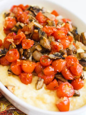 Close up of a white serving dish with creamy polenta topped with roasted mushrooms and tomatoes.