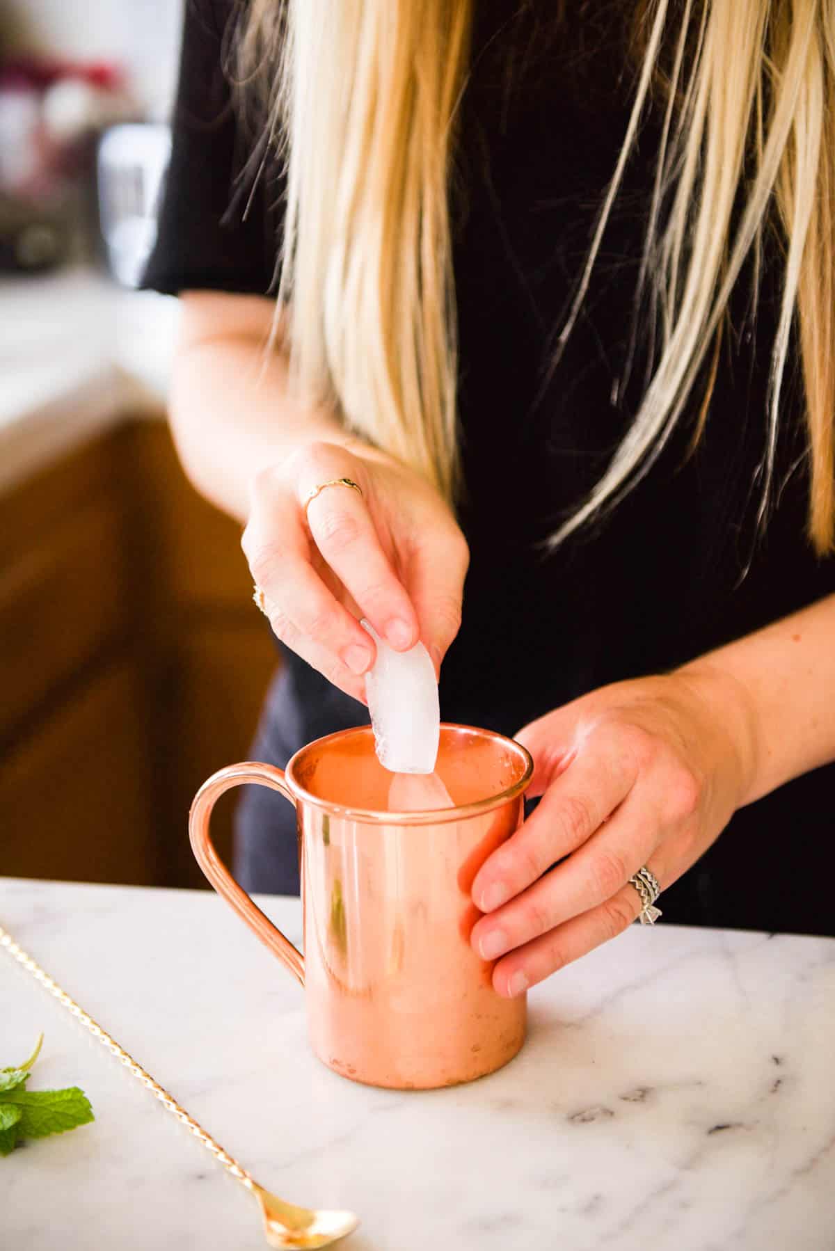Woman adding ice to a copper mug on a counter.