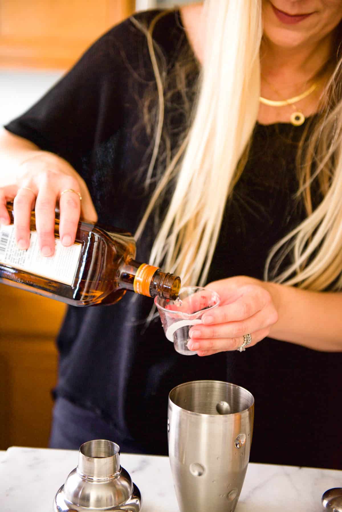 Woman measuring Cointreau into a cocktail shaker.