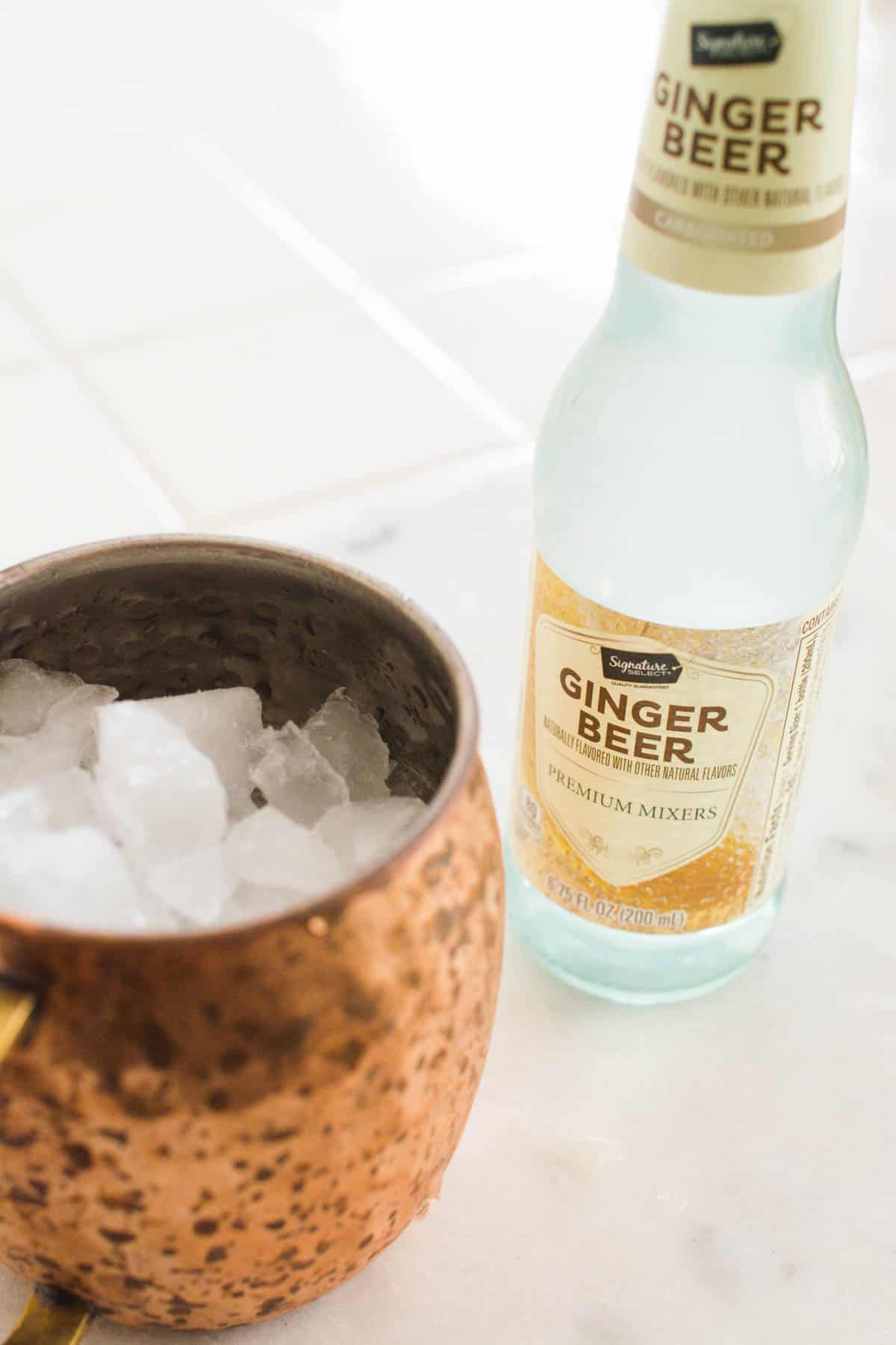 A copper mug full of ice next to a bottle of ginger beer.