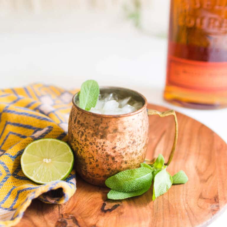 A copper mug with a Bourbon Mule with a bottle of bourbon in the background.