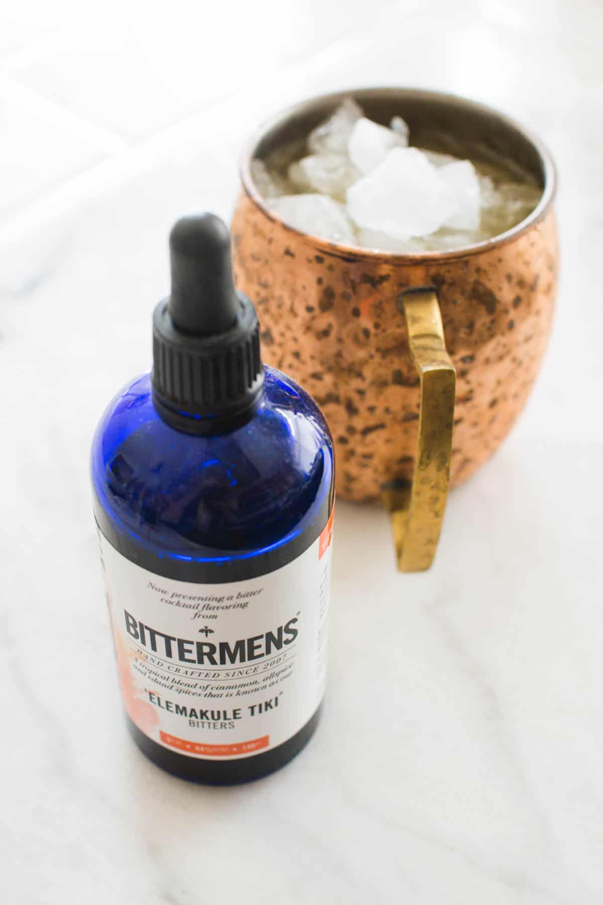 Close up of a bottle of bitters next to a copper Moscow Mule mug.