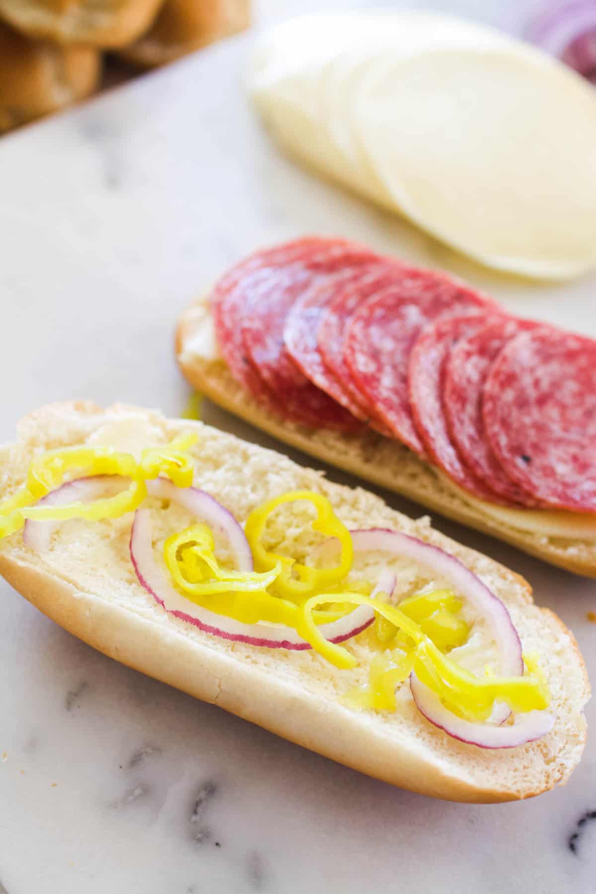 Red onions and pepperoncini pieces on one side of a roll with salami on the other.