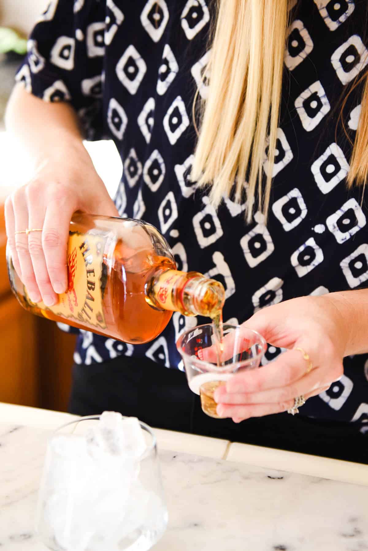 Woman measuring Fireball whiskey in a jigger.