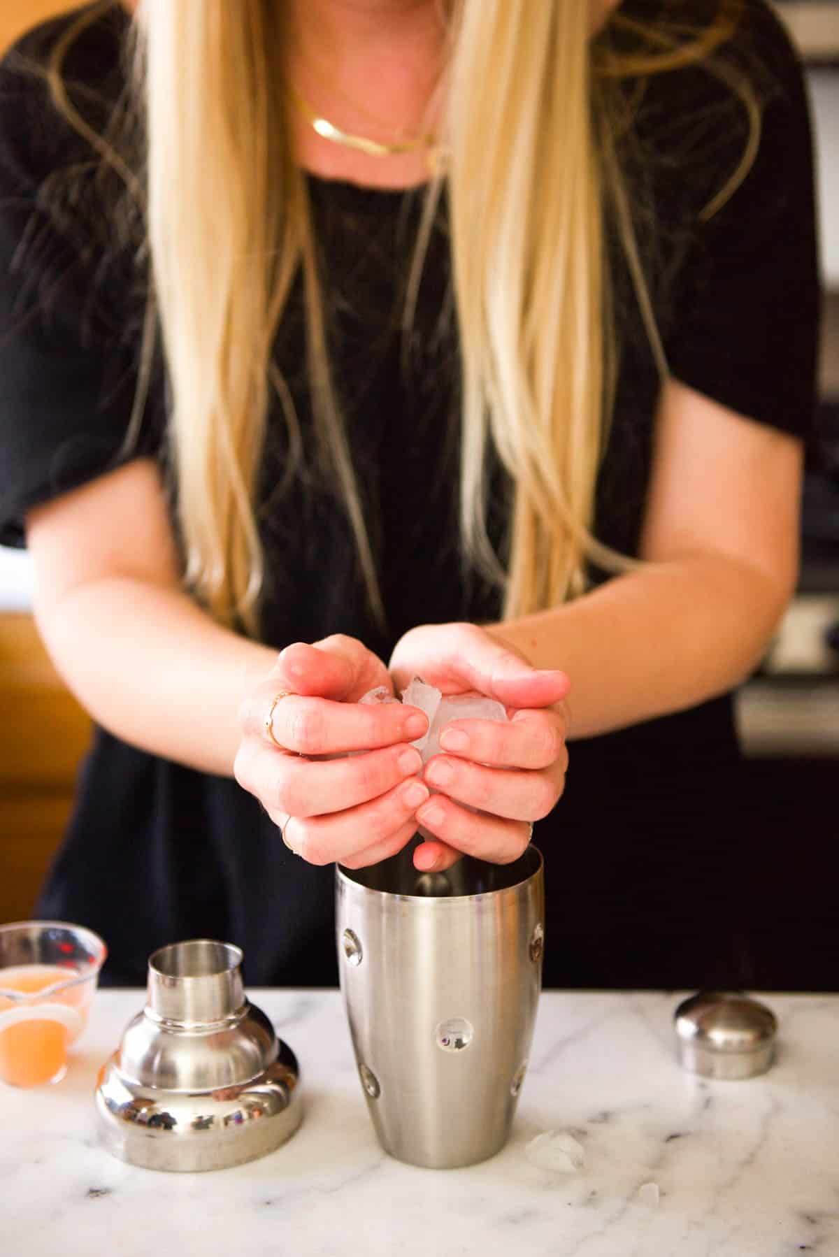 Woman adding ice to a cocktail shaker.