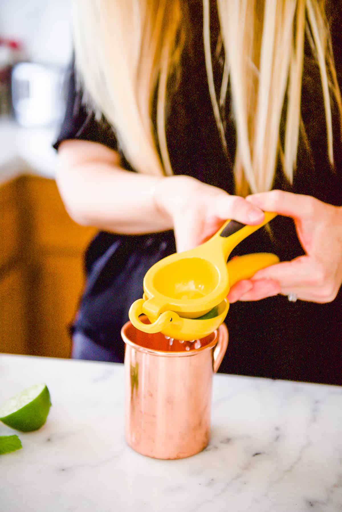 Woman squeezing lime juice into a copper mug.