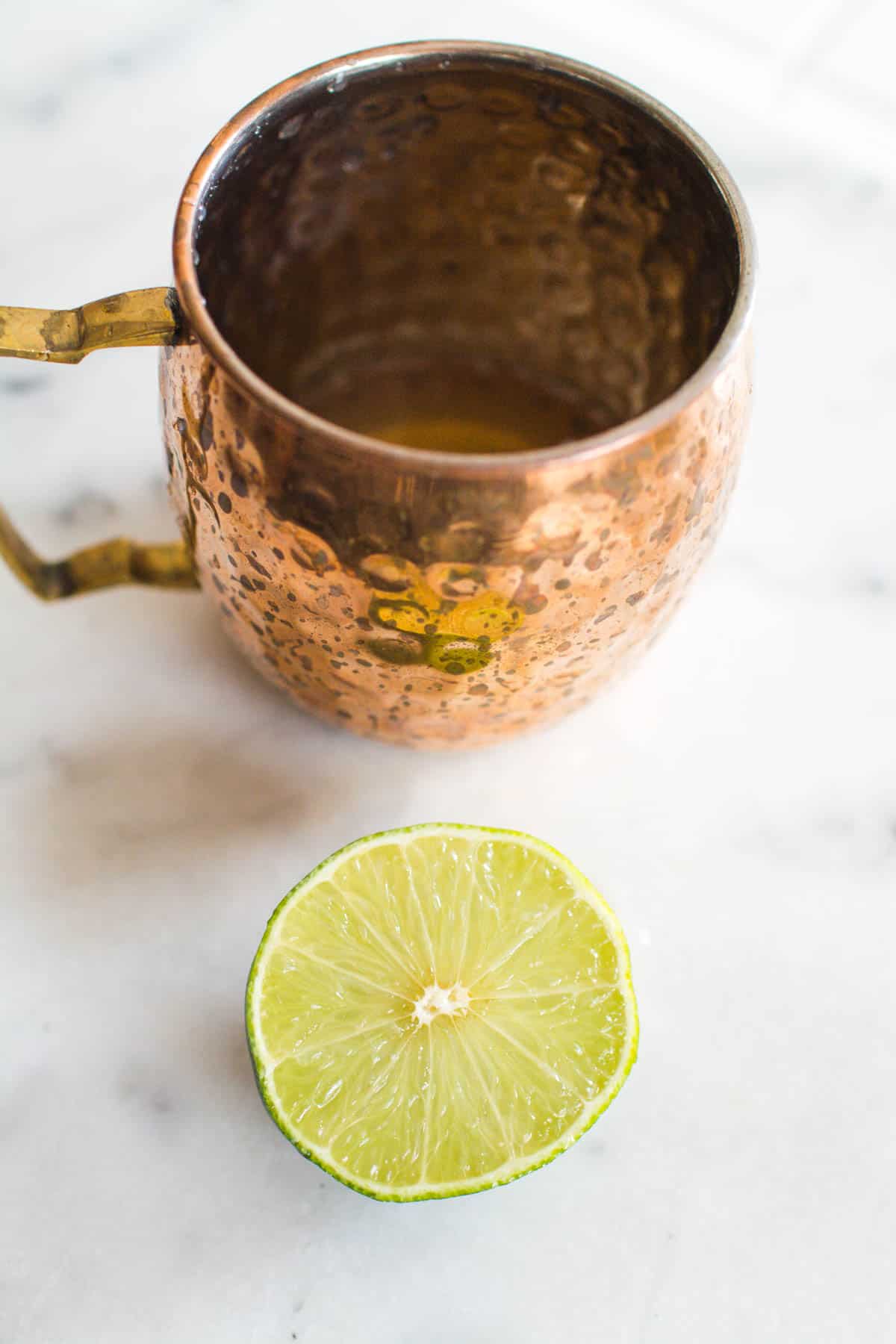 A copper Moscow Mule mug with a lime next to it.