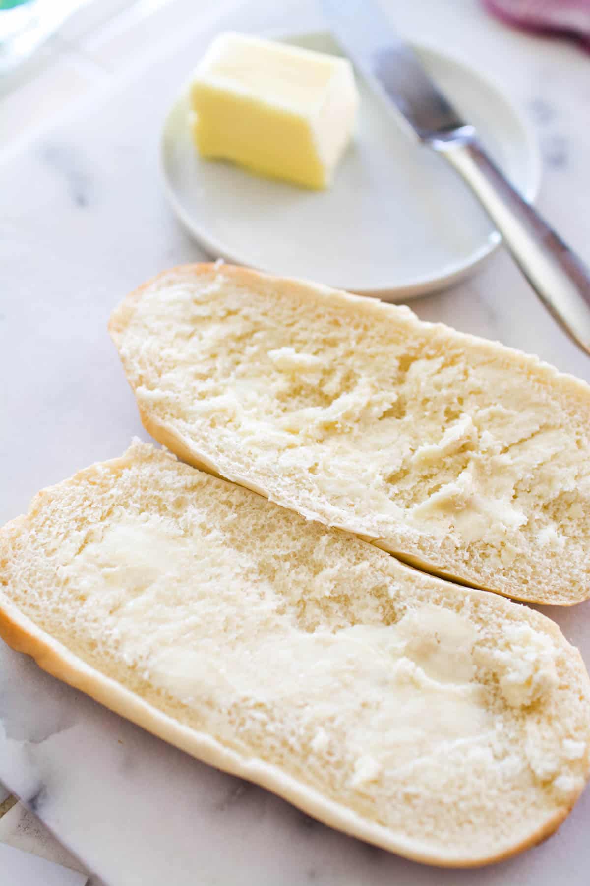 An open sandwich roll on a cutting board with butter spread on each side.