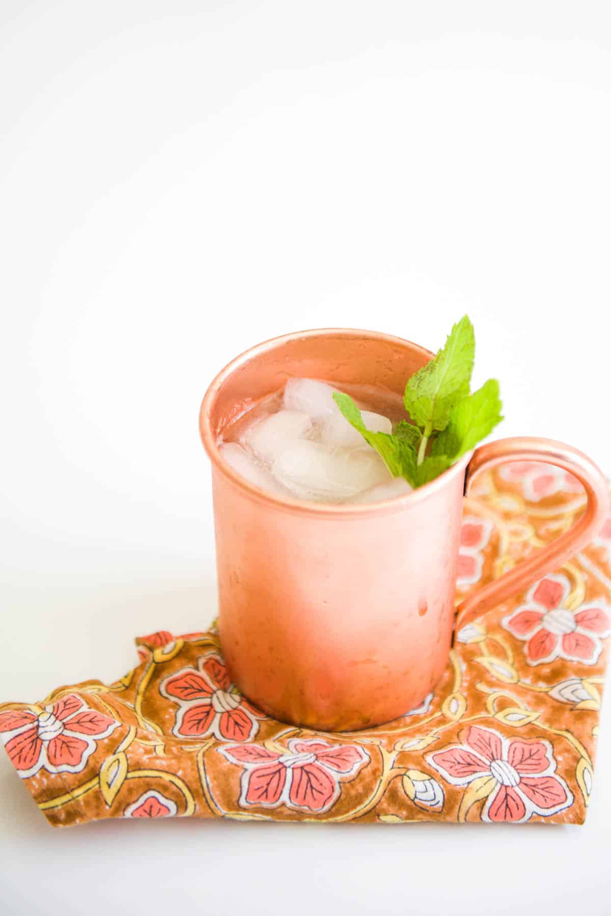 A fabric napkin on a table with a copper mug on top with a non alcoholic Moscow Mule in a copper mug on it.