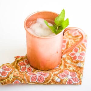 A copper mug on a patterned fabric napkin with a mint garnish in a Moscow Mule mocktail.