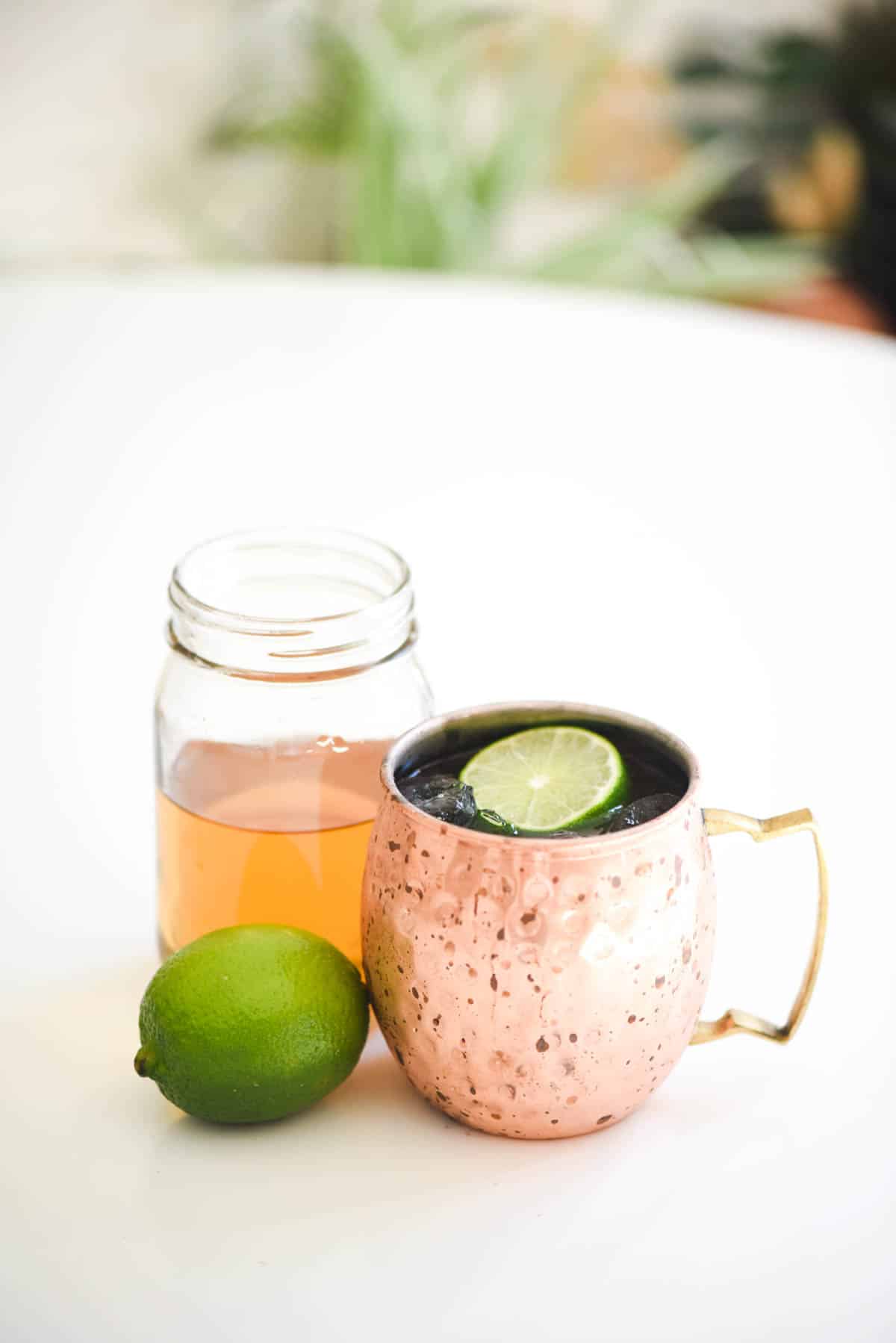 A vanilla moscow mule on a table in a copper mug with vanilla simple syrup in a jar on a table.