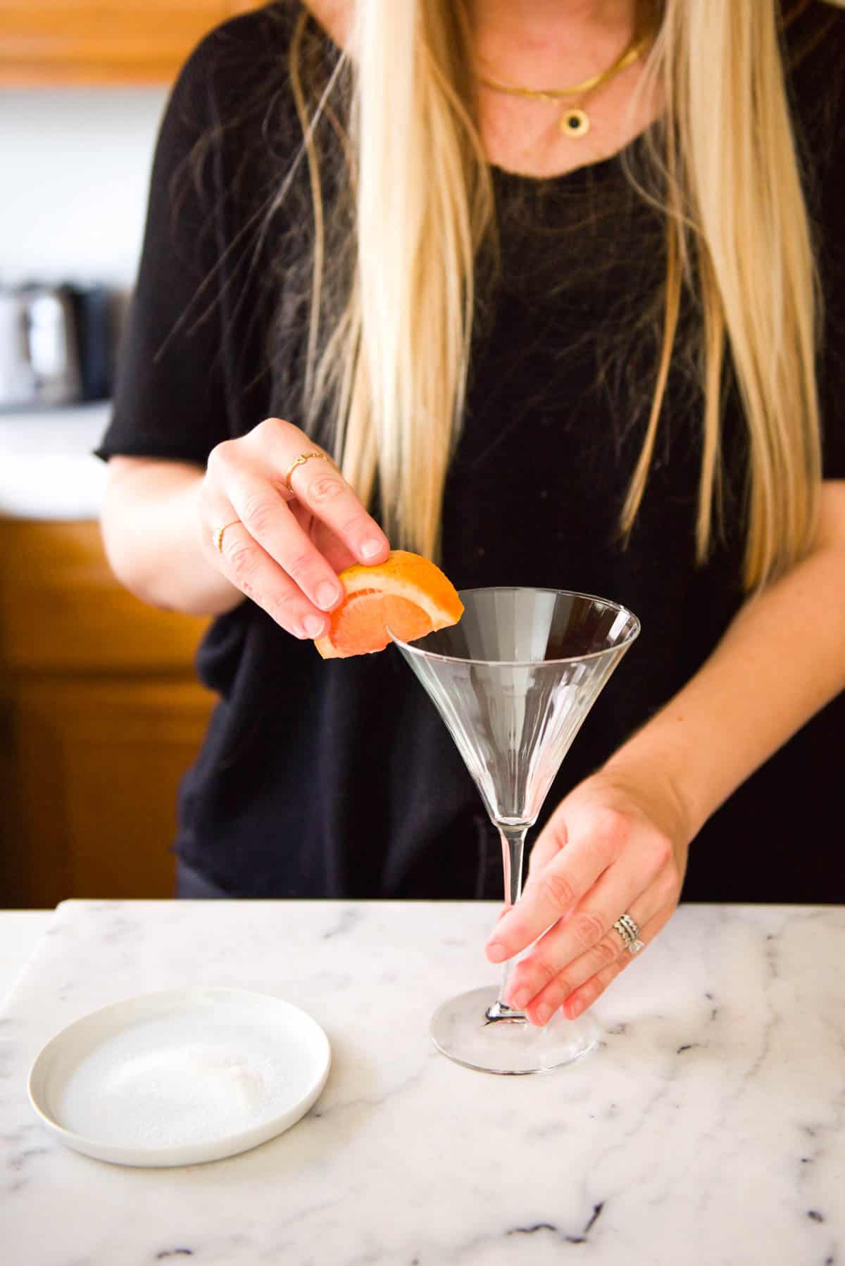 Woman rubbing a grapefruit slice on a martini glass rim.