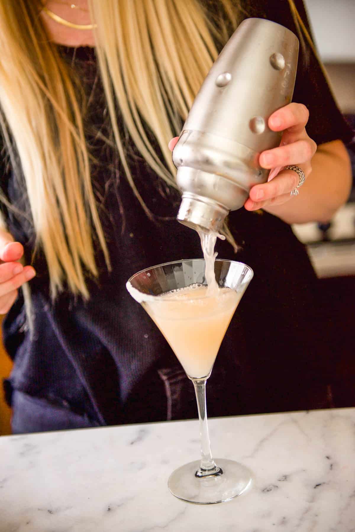 Pouring a martini into a martini glass on a table.