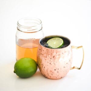 A copper moscow mule mug on a table next to a jar of vanilla simple syrup.