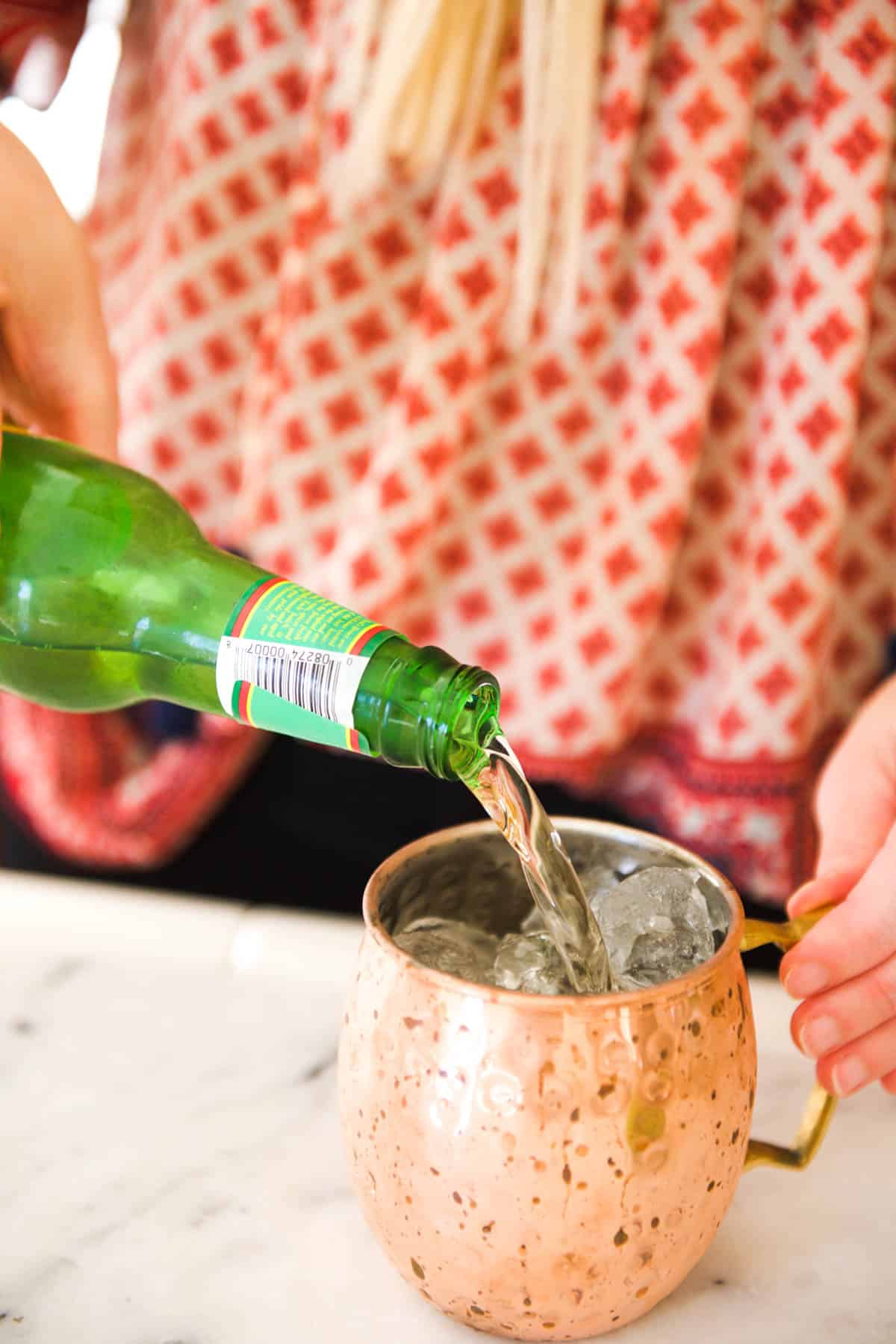 Woman adding ginger beer to a copper mug mule.