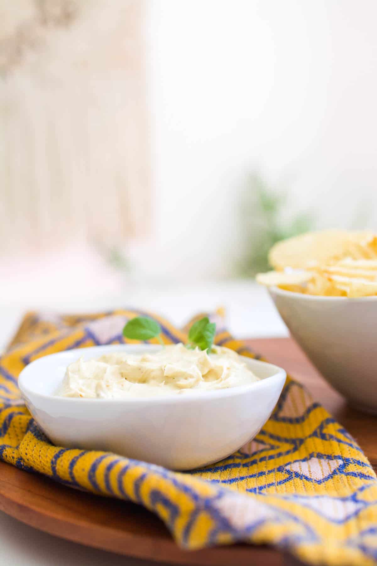 A bowl of dip next to a bowl of chips on a table.