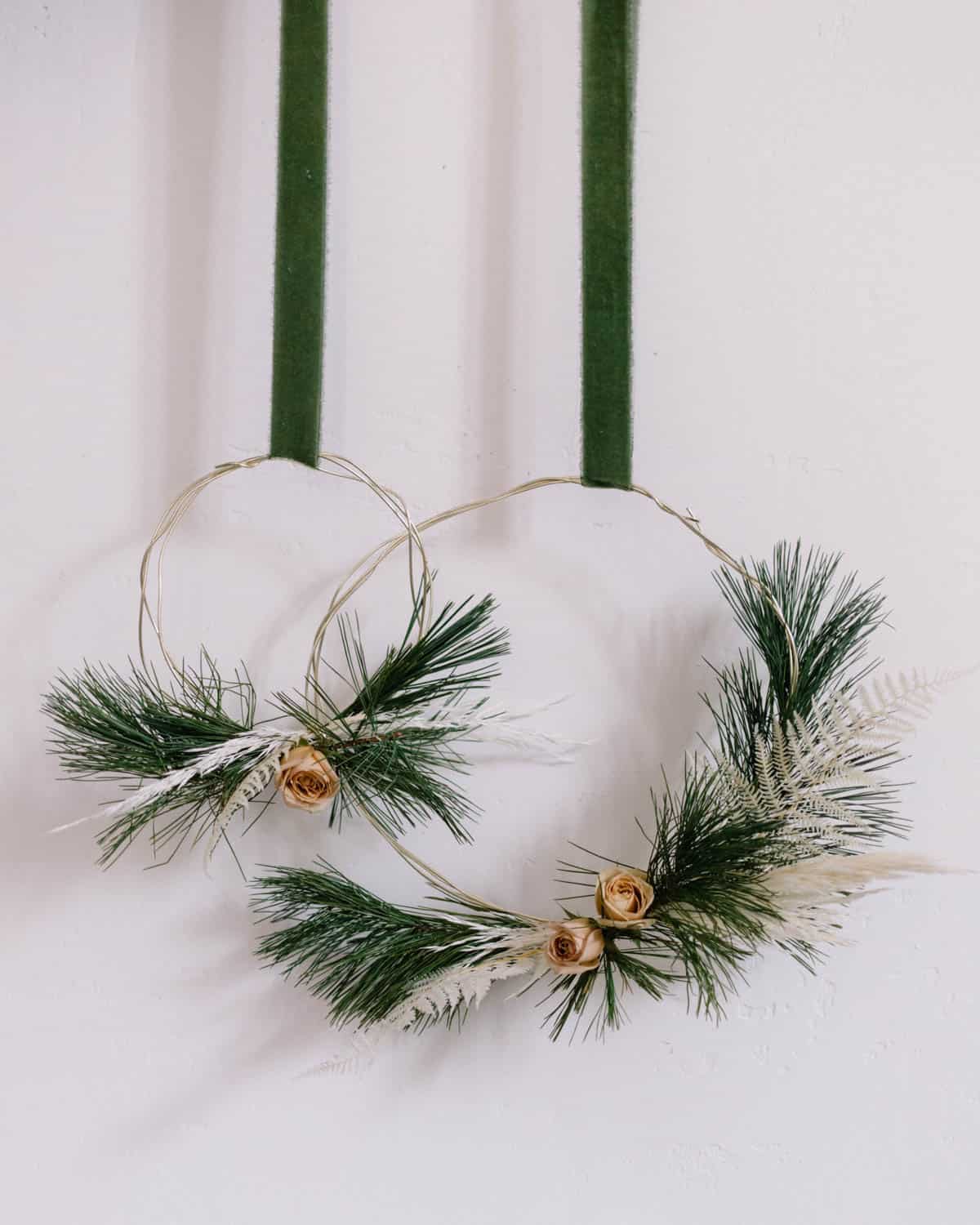 To modern holiday wreaths hanging on a wall by green ribbon.