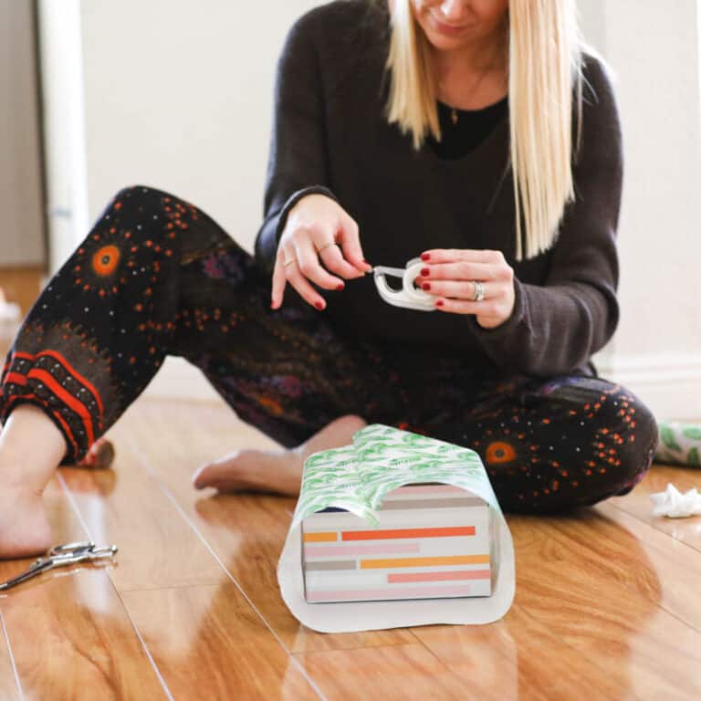 Woman sitting on the floor wrapping a holiday present.
