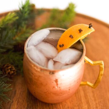 Close up image of a moscow mule in a copper mug, topped with a clove studded orange slice.