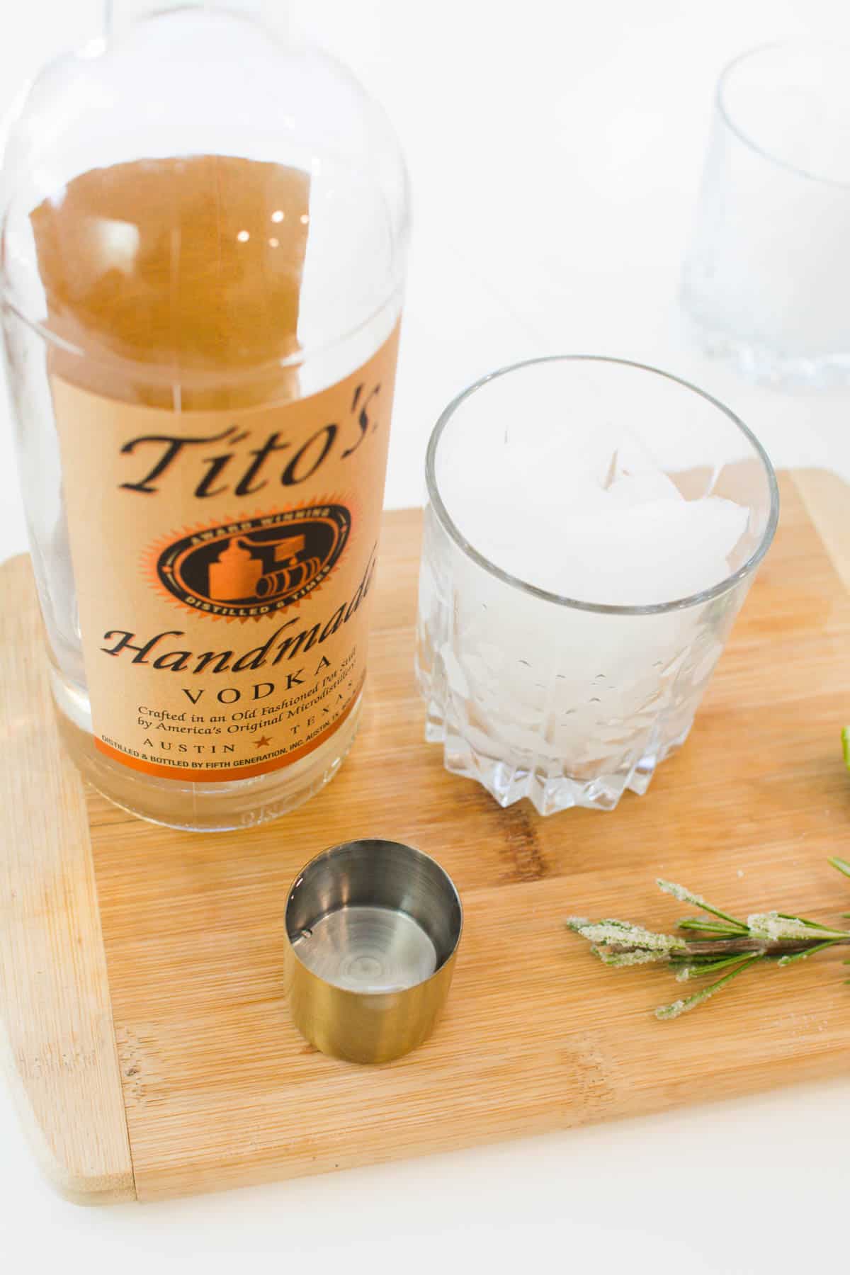 A jigger next to a bottle of Tito's vodka and a cocktail glass with ice.