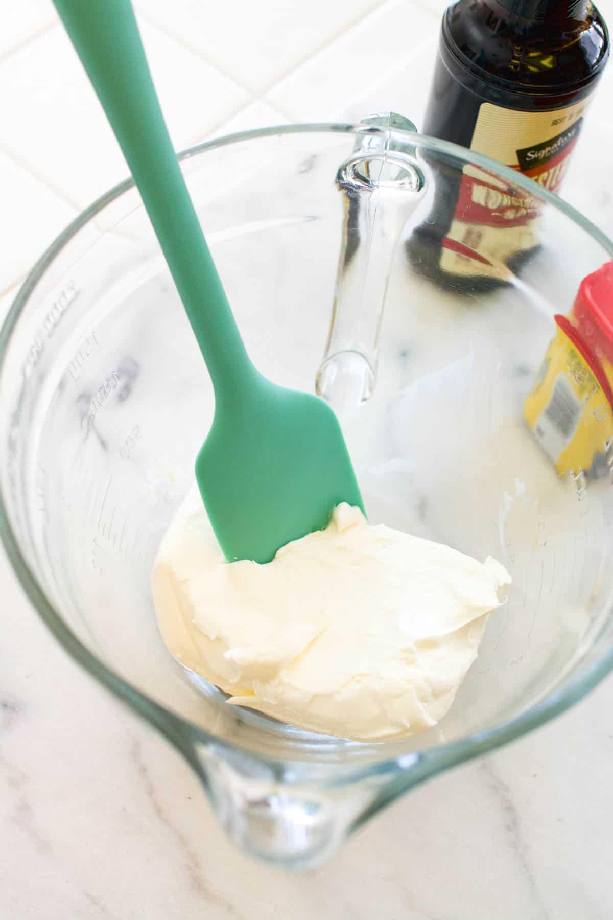 A glass bowl with cream cheese and a spatula in it.