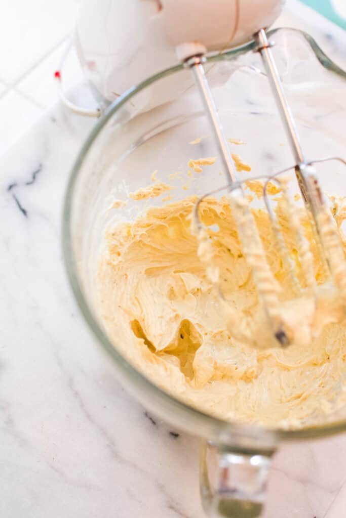 A glass bowl with a homemade chip dip being mixed by a hand mixer.