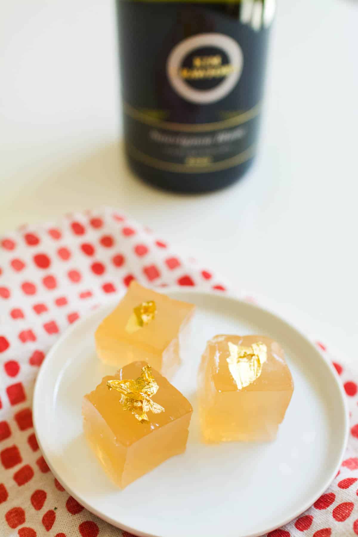 A small white dessert plate with 3 square pieces of jello topped with edible gold leaf.