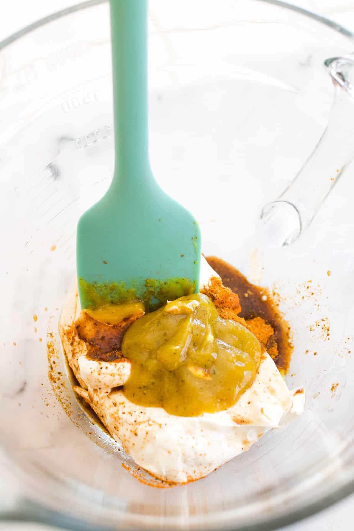 A glass bowl with cream cheese and colorful spices in it next to a spatula.