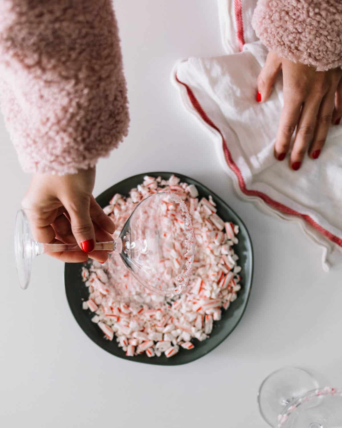 Crushed candy canes on a plate being used to rim a cocktail glass.