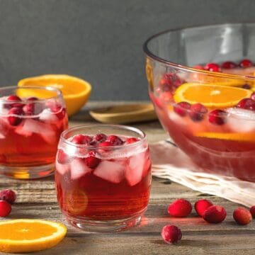 A glass punch bowl with a red punch in it next to a glass of punch.
