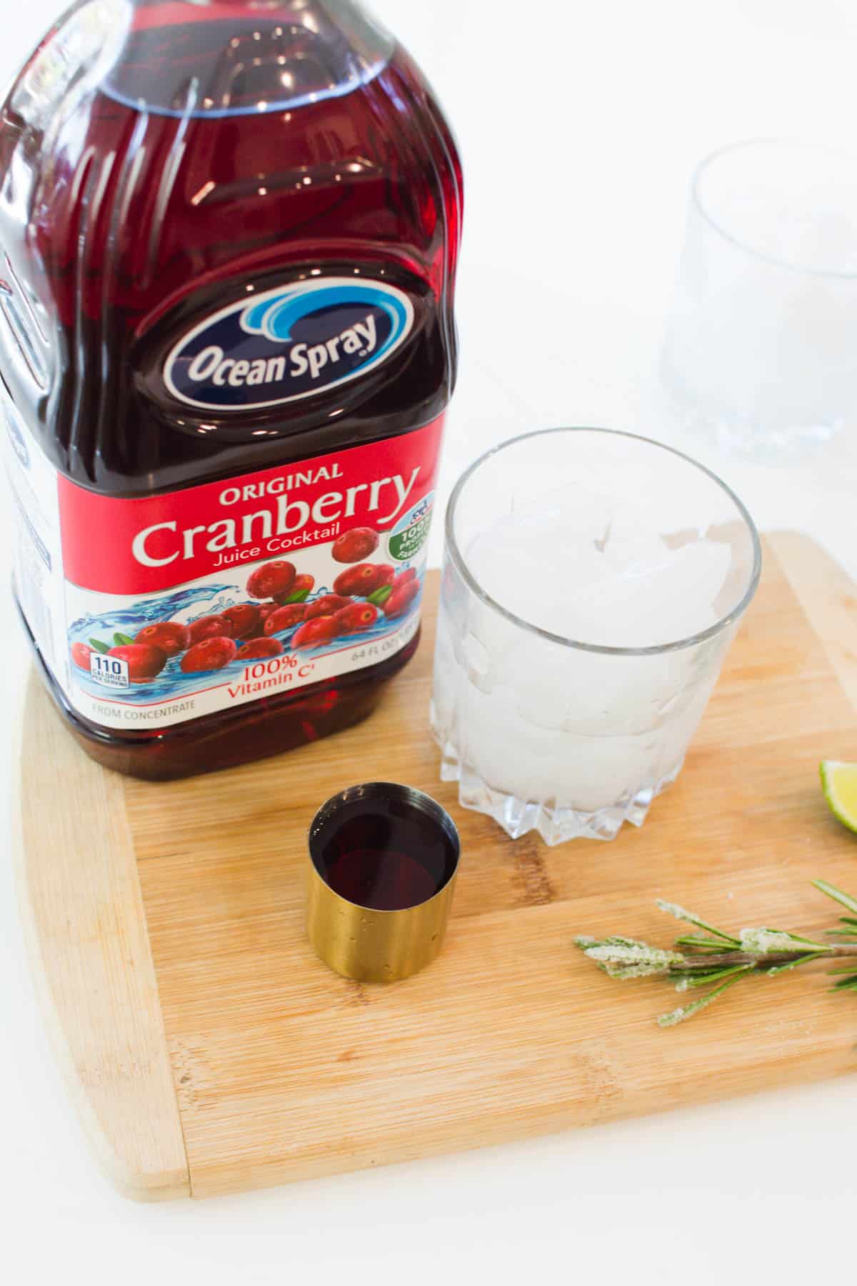 A cocktail glass full of ice next to a jigger with cranberry juice.