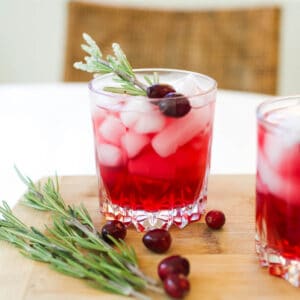 A cocktail glass with vodka and cranberry garnished with lime and cranberries on a table.