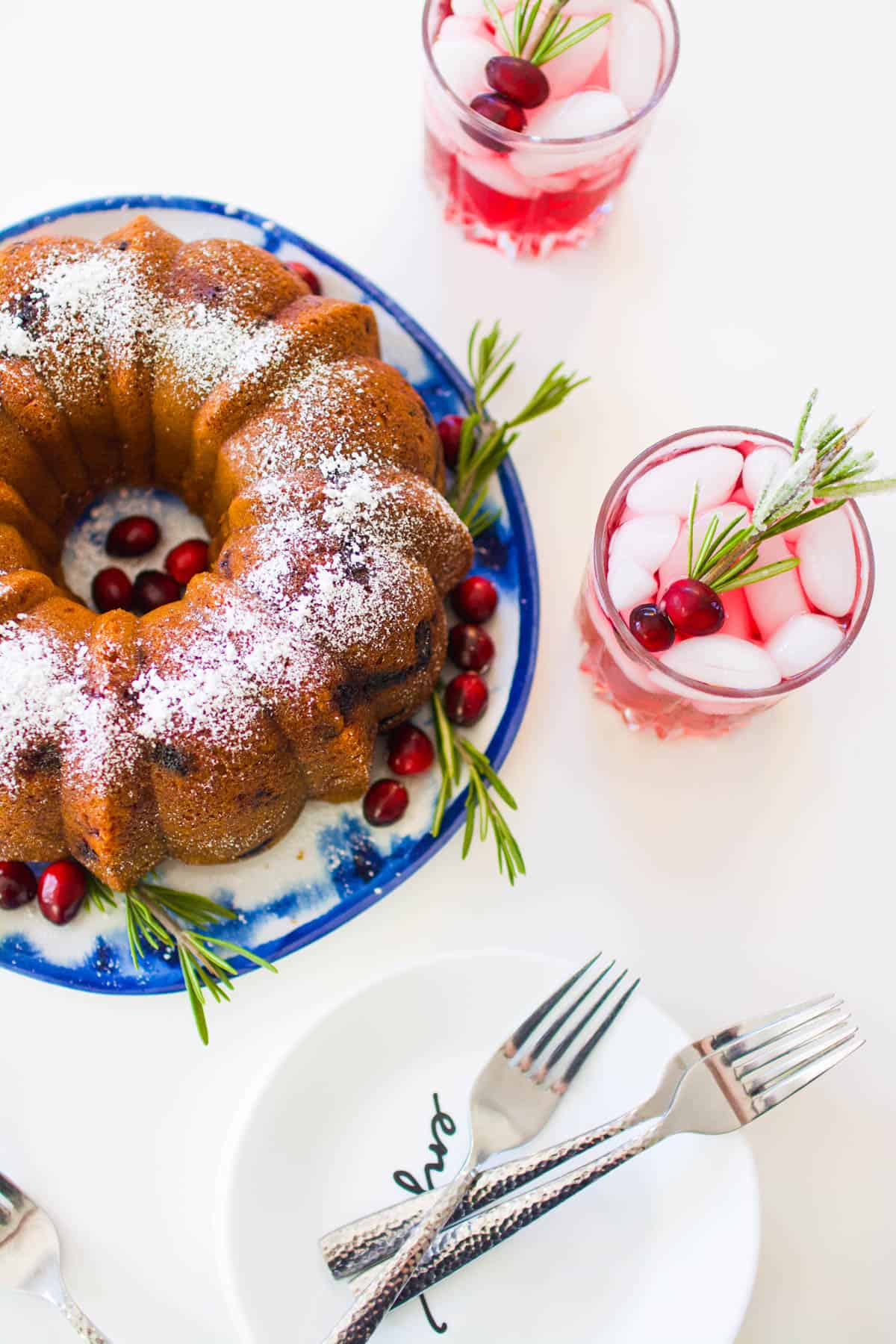 Overhead view of a bundt cake topped with powdered sugar next to cranberry vodka in glasses.