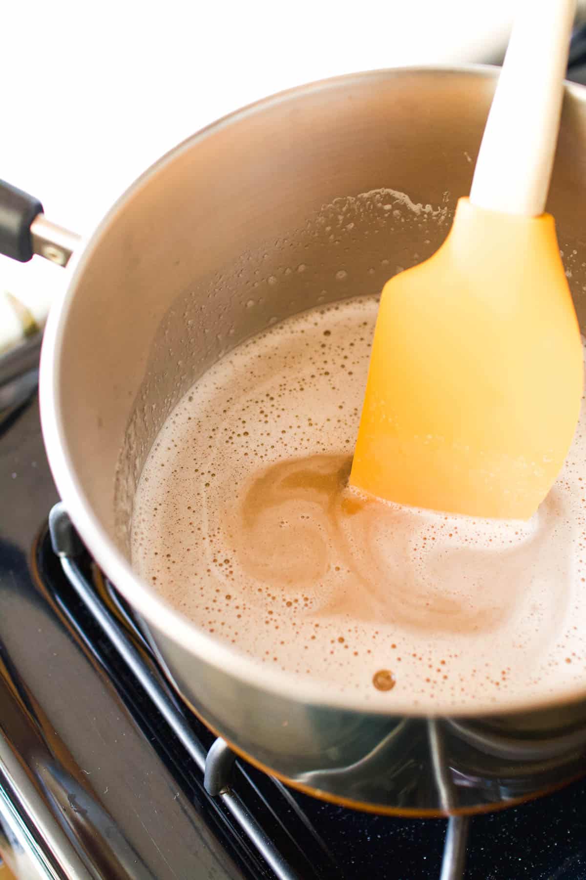 A spatula stirring a liquid mixture in a saucepan.