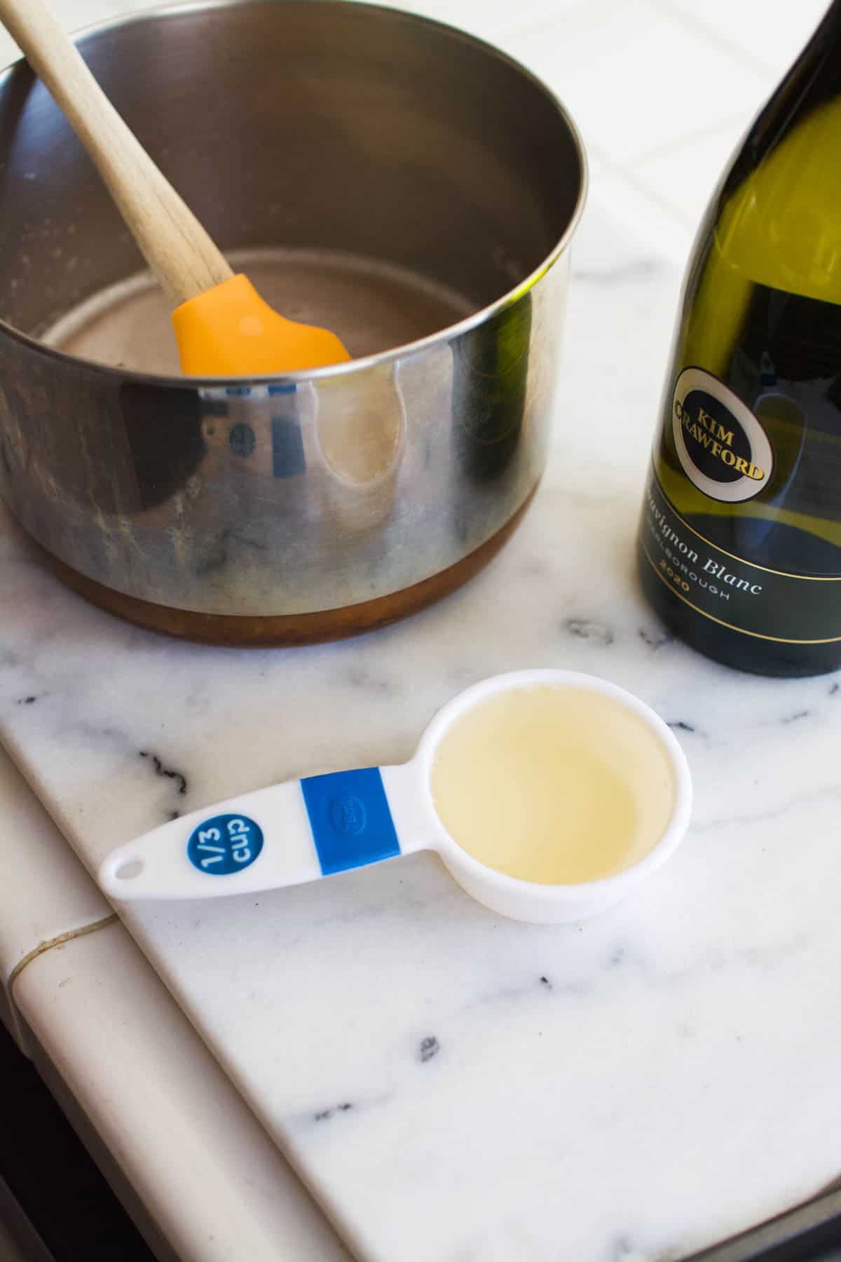 A measuring cup of sauvignon blanc next to a saucepan on a counter.