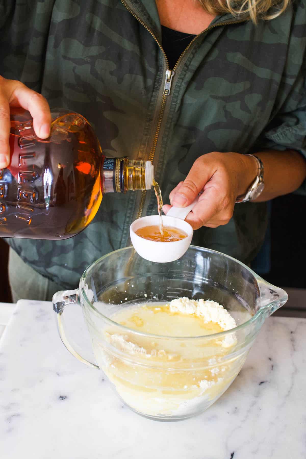 A woman pouring bourbon into a measuring cup above a batter bowl.