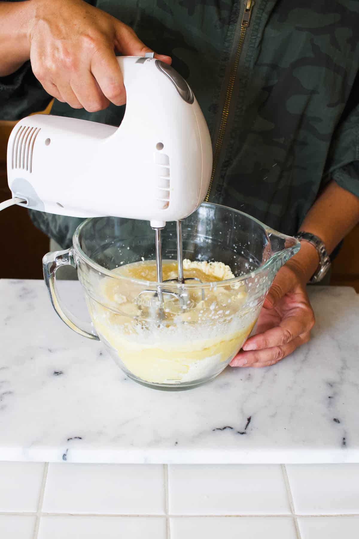 Woman mixing cake batter in a glass batter bowl with a hand mixer.