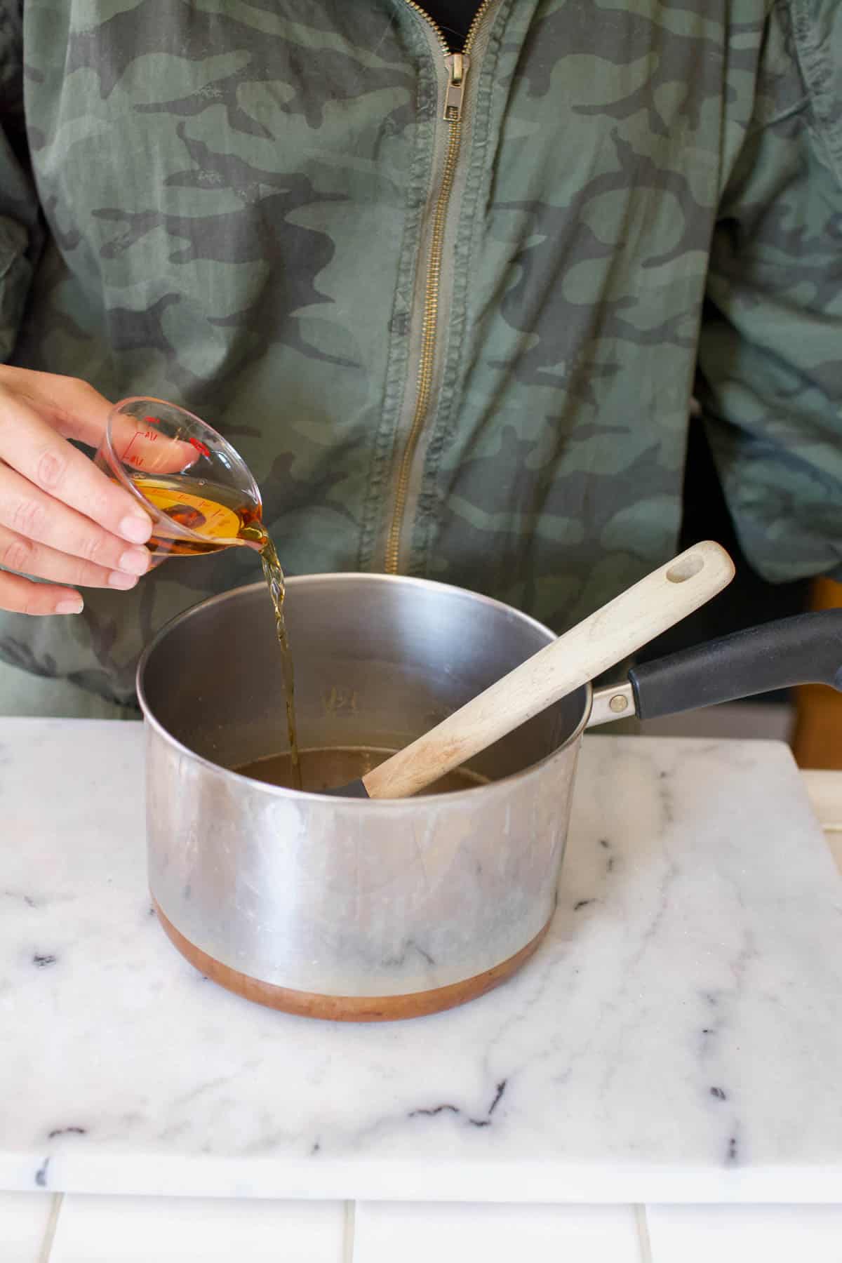 Woman adding bourbon to a saucepan.